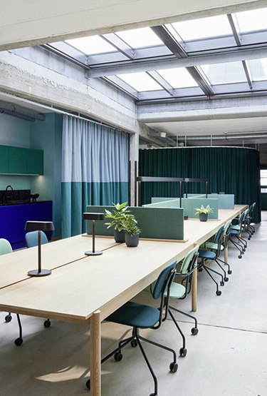 Przestrzeń coworkingowa z długim stołem i tapicerowanymi krzesłami na kółkach w morskiej kolorystyce.